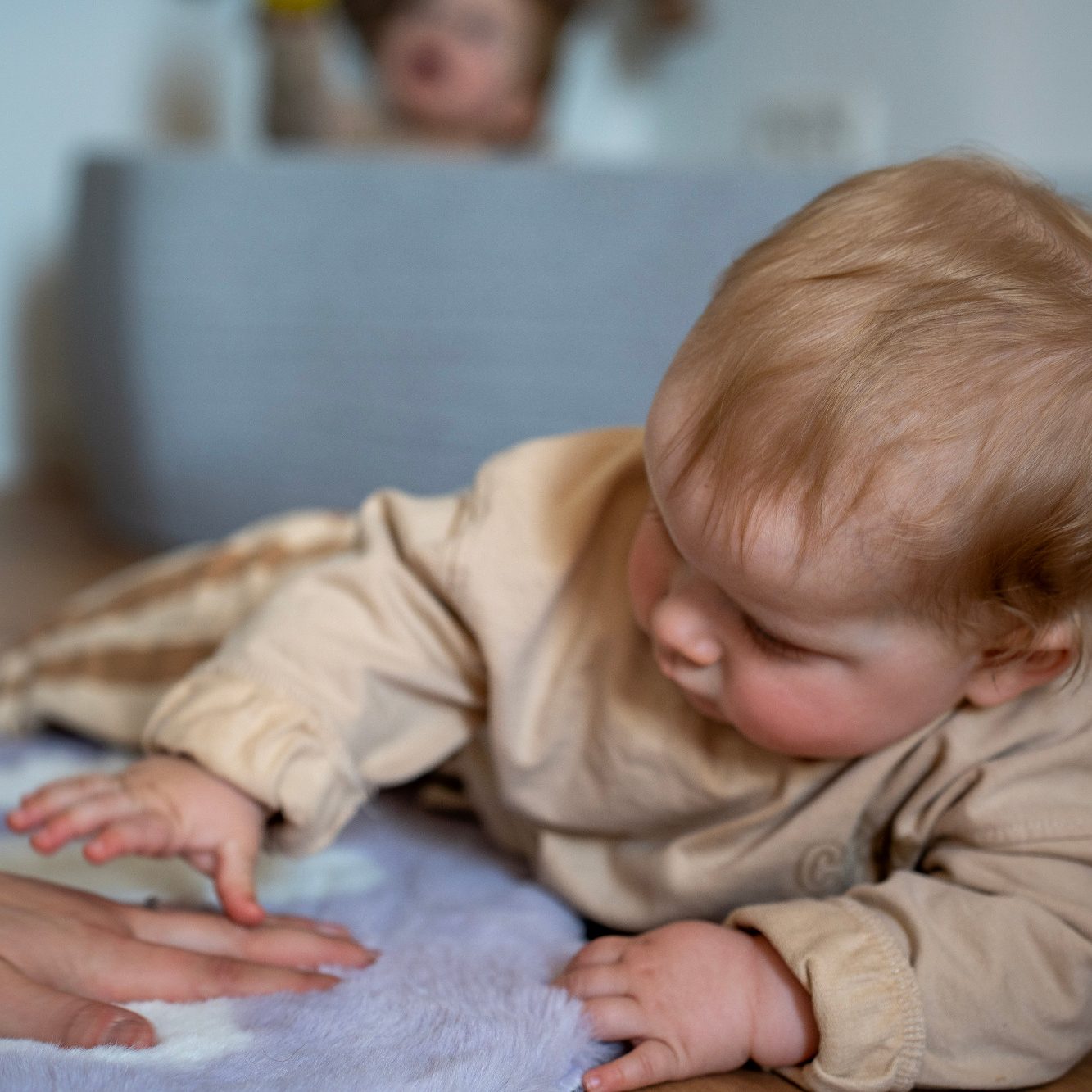 Ein Baby streckt die Hand nach einer anderen Hand auf einem weichen Stoff.
