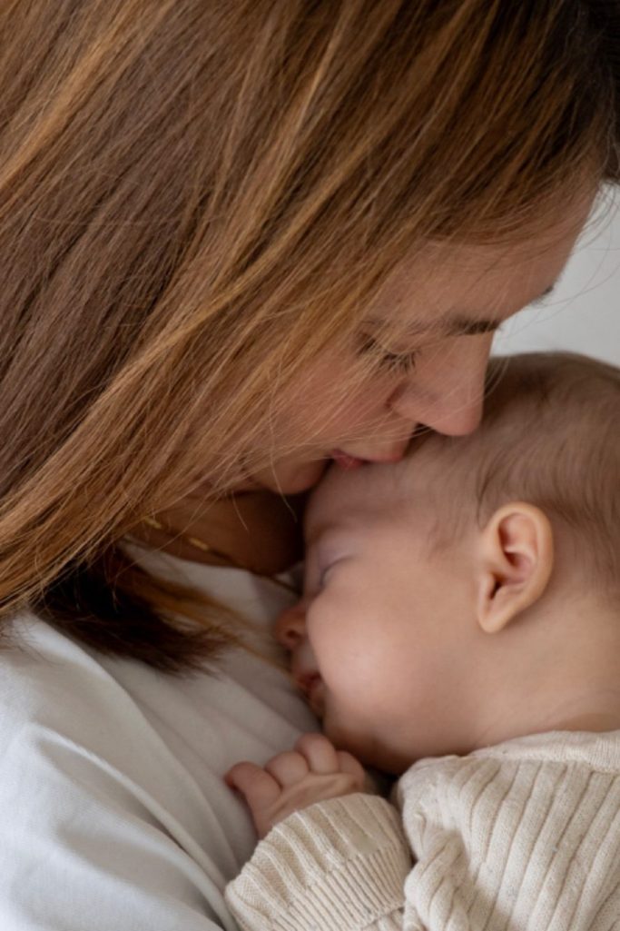 Familienfotografie Frau mit langen Haaren lächelt, während ein kleines Kind ihr von hinten umarmt.