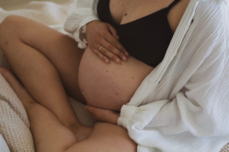 Schwangere Person mit einem sichtbaren Bauch, gebettet in einer ruhigen, häuslichen Umgebung.