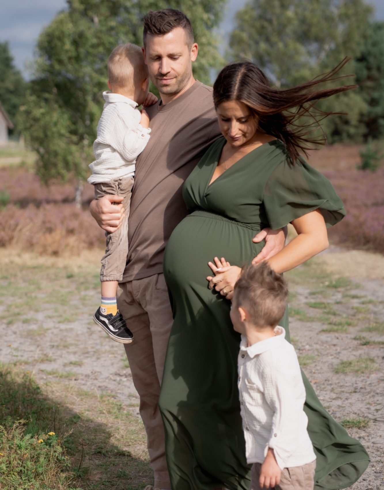 Newbornfotografie Schwangere Frau in einem weißen Oberteil, die sanft ihren Bauch hält.