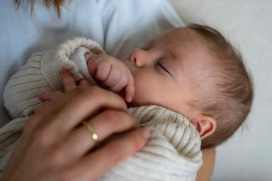 Schlafendes Baby in einem weißen Strickpullover, sanft gehalten von einer Hand.