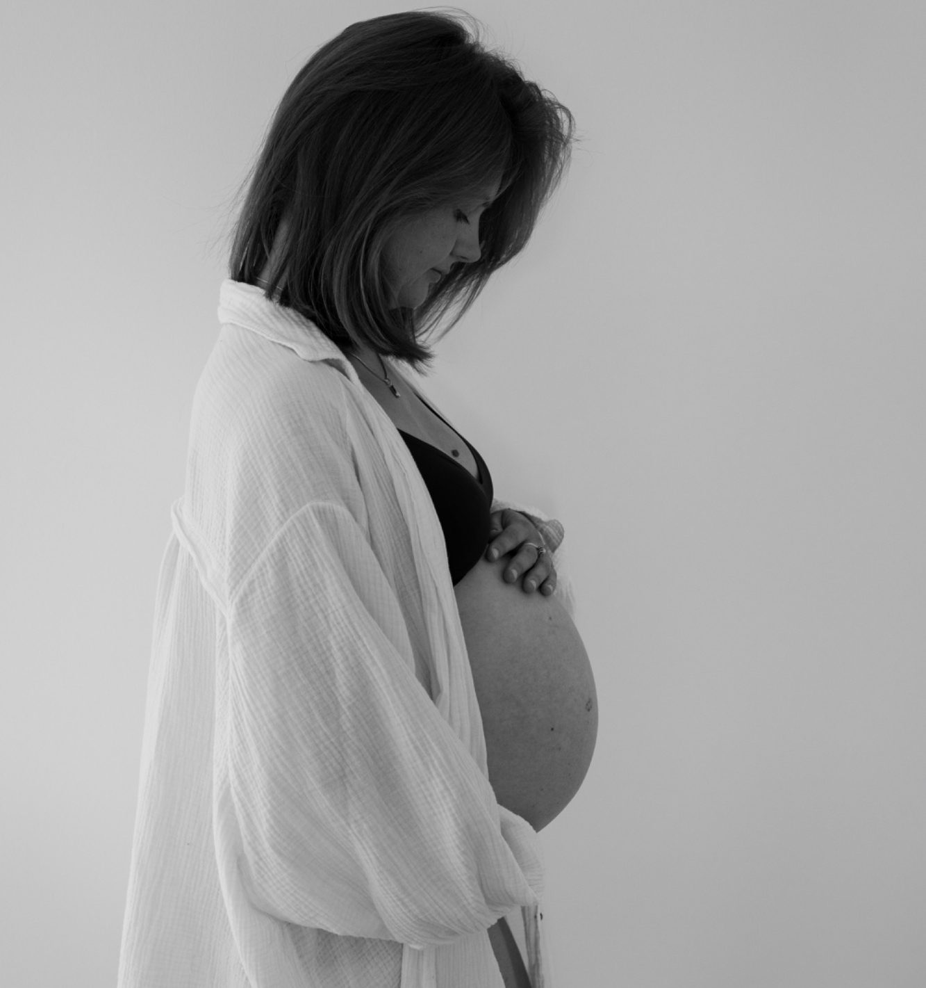 Schwangere Frau in einem weißen Oberteil, die sanft ihren Bauch hält.