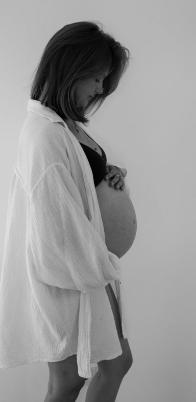 Schwangere Frau in einem weißen Kimono, die sanft ihren Bauch hält.