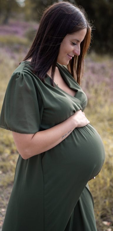Schwangere Frau mit lächelndem Gesicht, die ihren Bauch sanft hält.