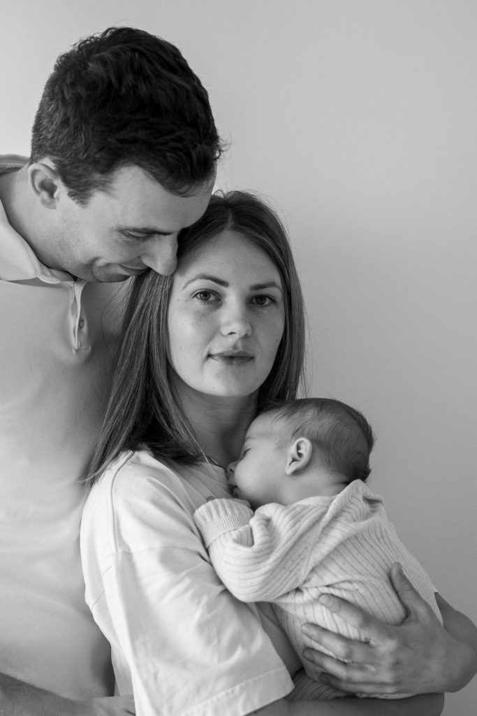 Ein Vater hält seine Partnerin und ein Baby in einer liebevollen Umarmung.