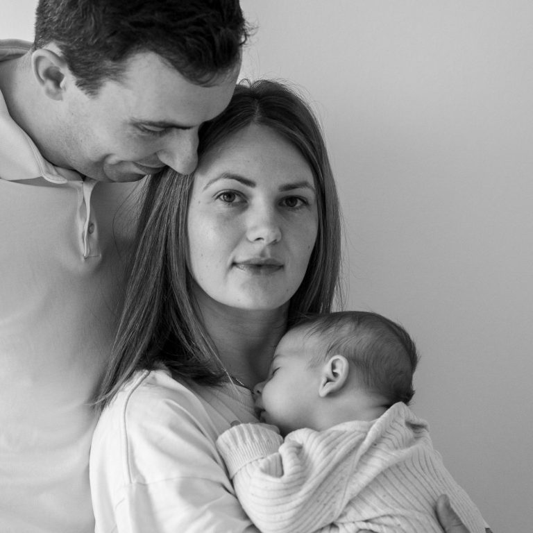 Familie mit einem Baby, Mutter hält es, Vater schaut liebevoll.