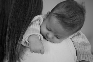 Ein Baby schläft friedlich auf der Schulter eines Erwachsenen.