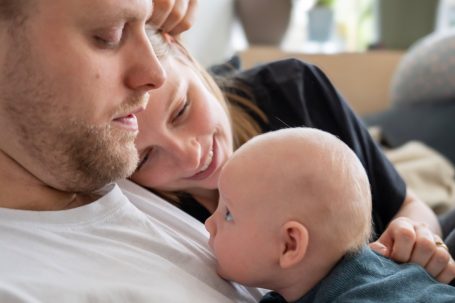 Ein Vater und eine Mutter betrachten liebevoll ihr Baby in einem häuslichen Umfeld.