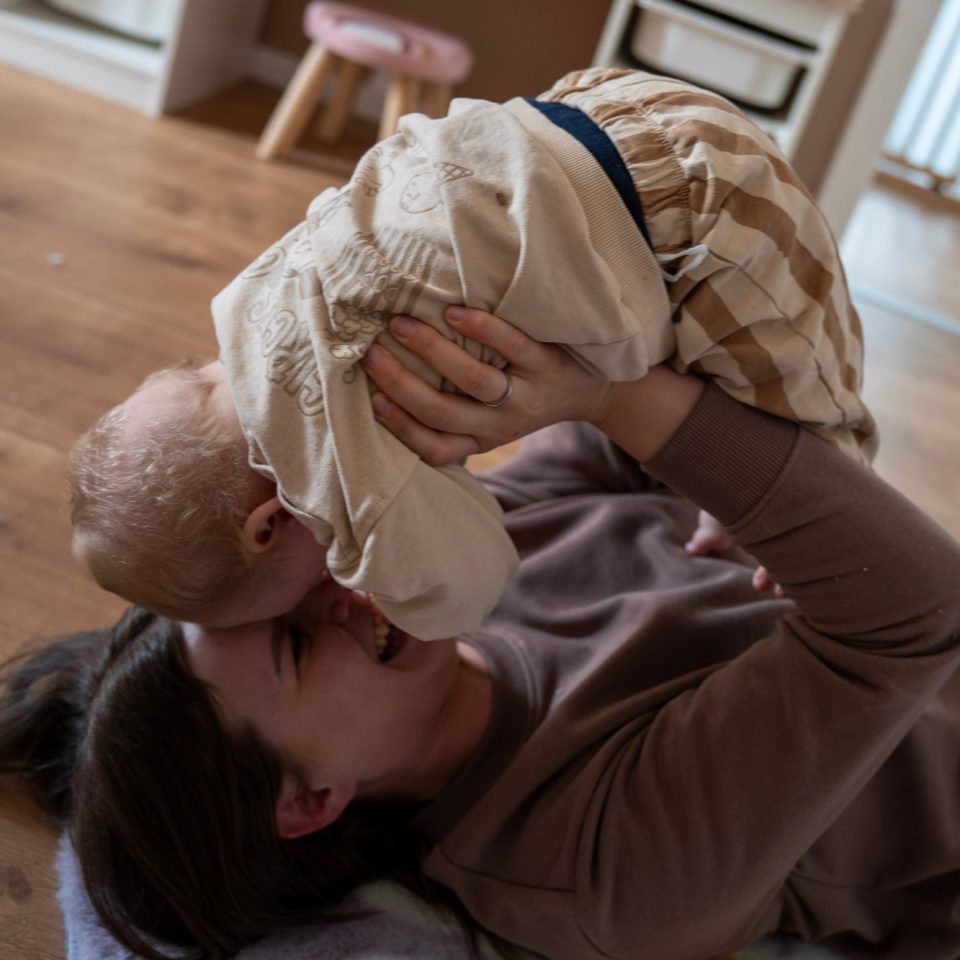 Eine Mutter hebt ihr lächelndes Kind spielerisch über sich.
