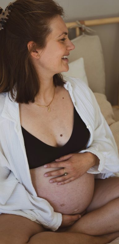 Schwangere Frau mit lächelndem Gesicht, die ihren Bauch sanft hält.