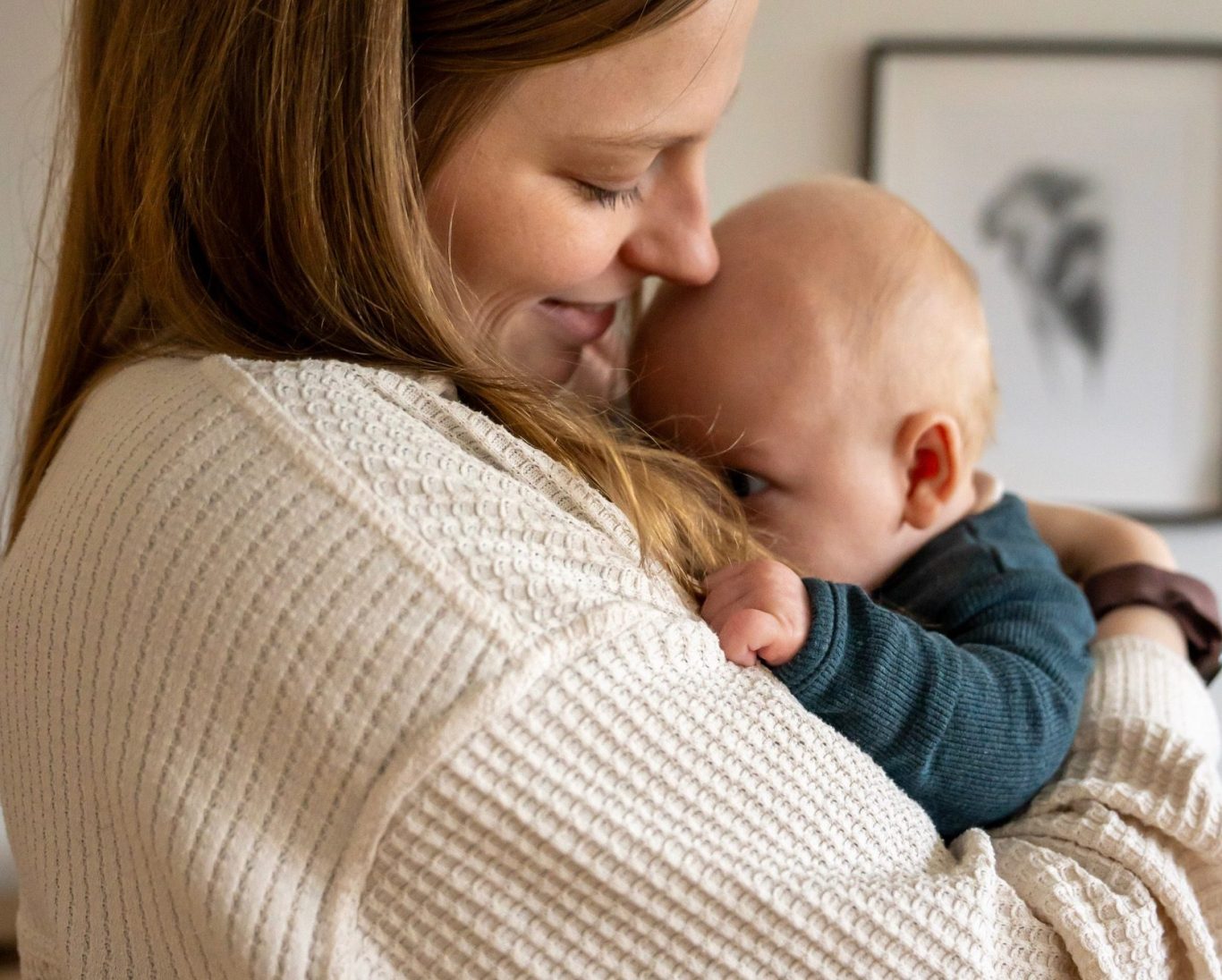 Frau hält ein Baby an ihrer Brust und lächelt dabei sanft.